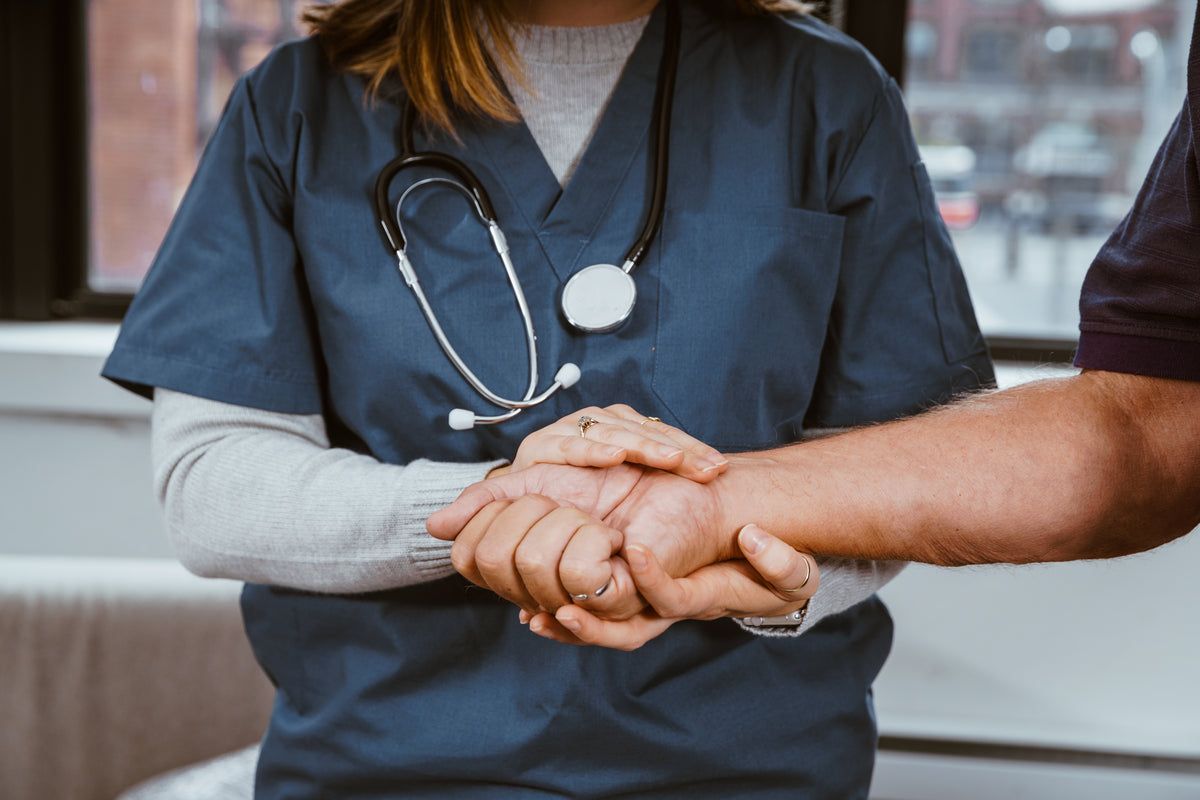 A female nurse holding a patient's hand.