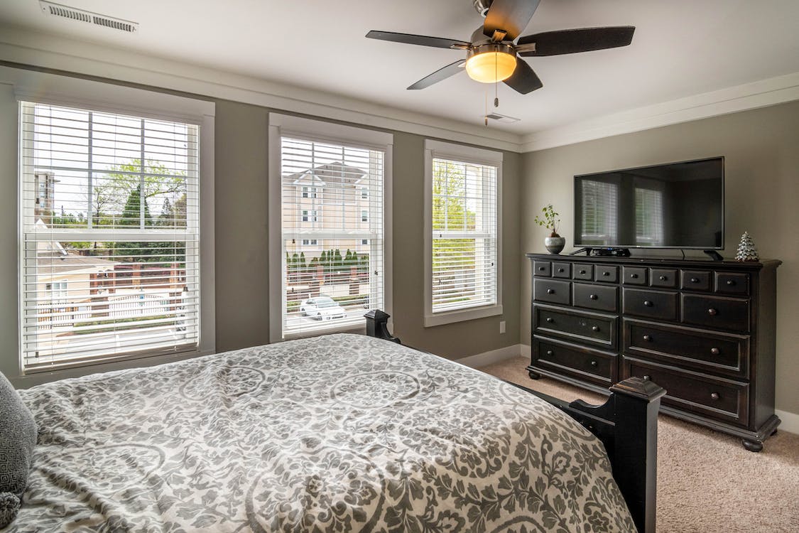 A bedroom with a television mounted on a wooden drawer.