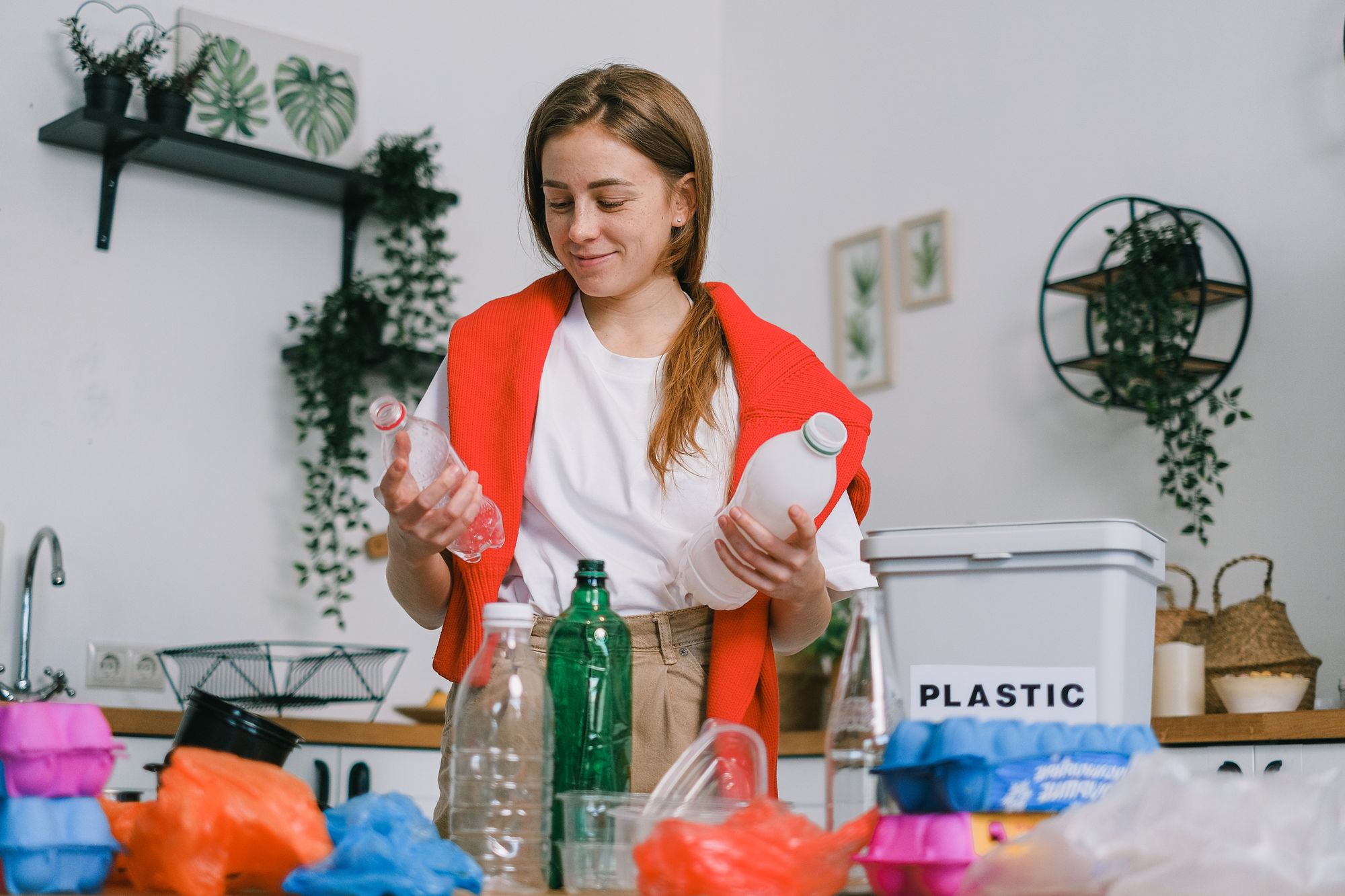 A woman organizing plastic trash with a trash can.